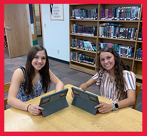 Two girls use tablets in a library